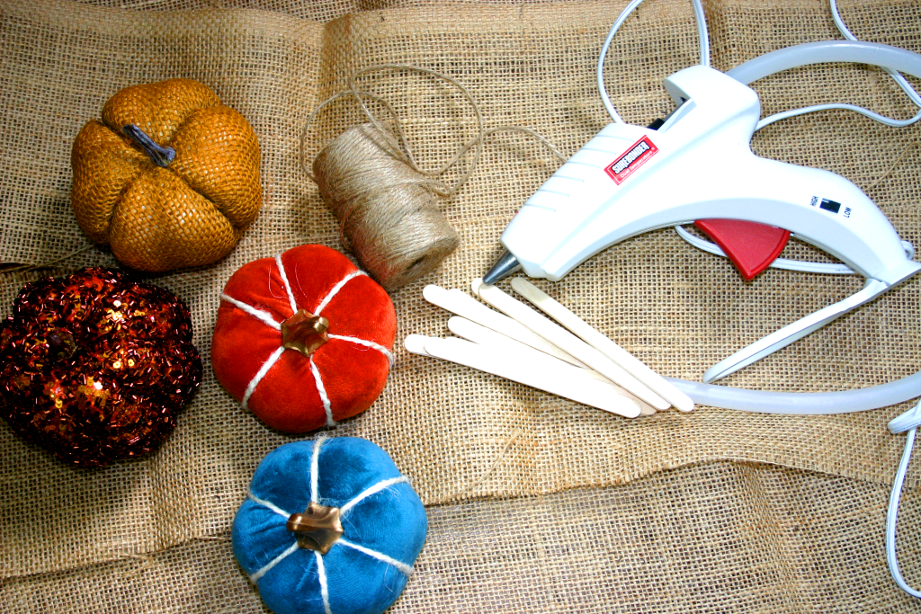pumpkins, hot glue gun, hot glue sticks, and twine laying on burlap