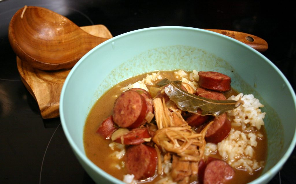 Blue bowl of chicken and sausage gumbo with a wooden spoon