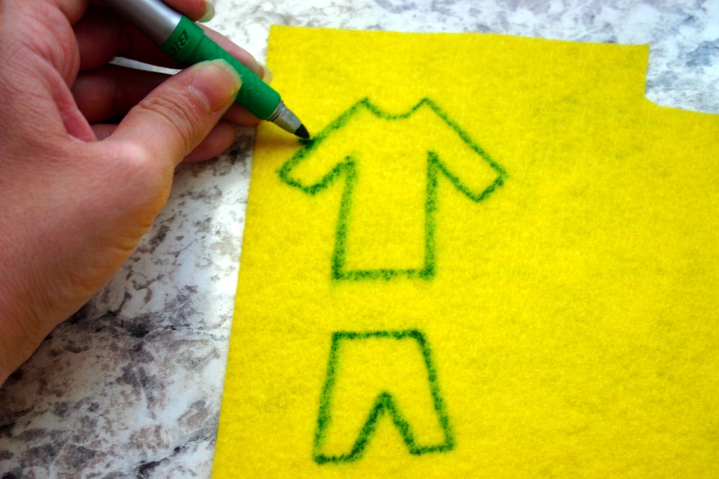 a hand using a marker to draw clothes on yellow felt fabric